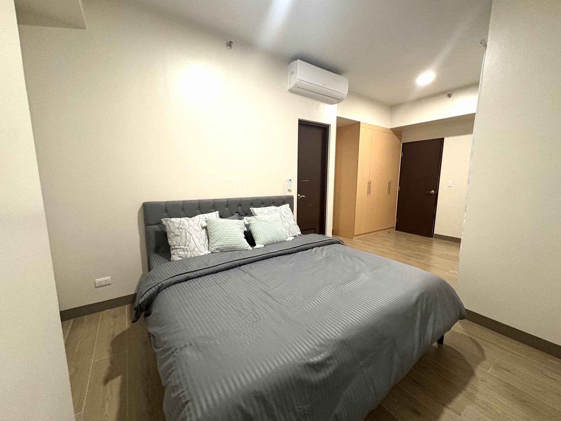 Primary bedroom of the DAYON TA condo, with a queen bed, wood floors, and a corner balcony door letting in daylight over Mactan Newtown